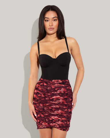 Model wears Cross Mesh Mini Shapewear Cover-Up Skirty - Cranberry Floral and one piece bombshell swimsuit