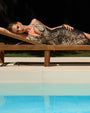 Editorial image of model wearing Ruched Sheer Maxi Skirty - Natural Snake paired with matching swimsuit laying on a lounge chair by the pool