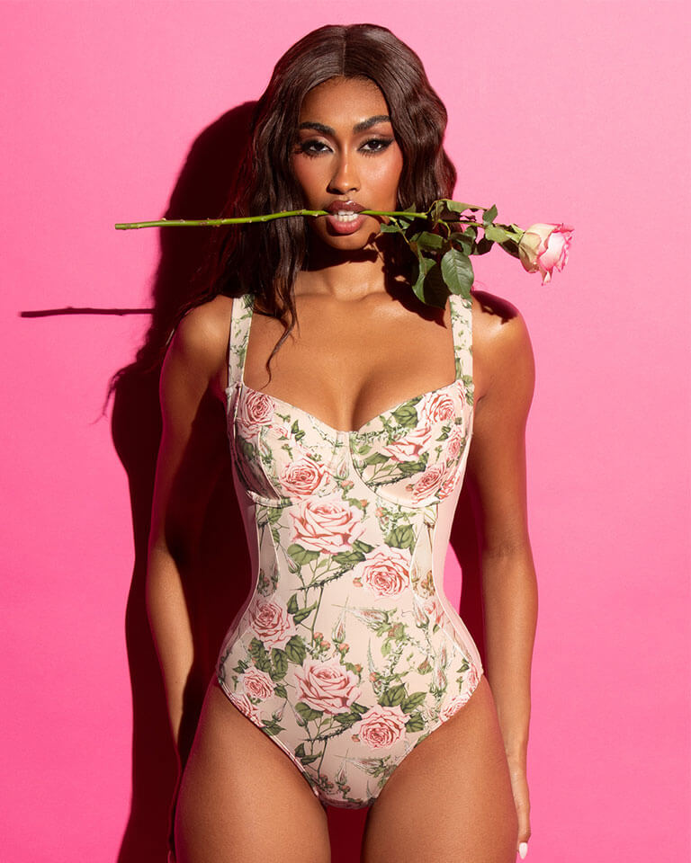 Woman wearing a floral swimsuit holding a rose against a pink background
